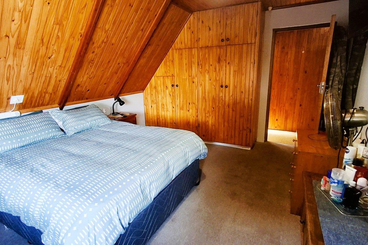 A bedroom featuring sloped timber ceilings, wood-paneled walls, and built-in wooden cabinetry, offering a rustic aesthetic.