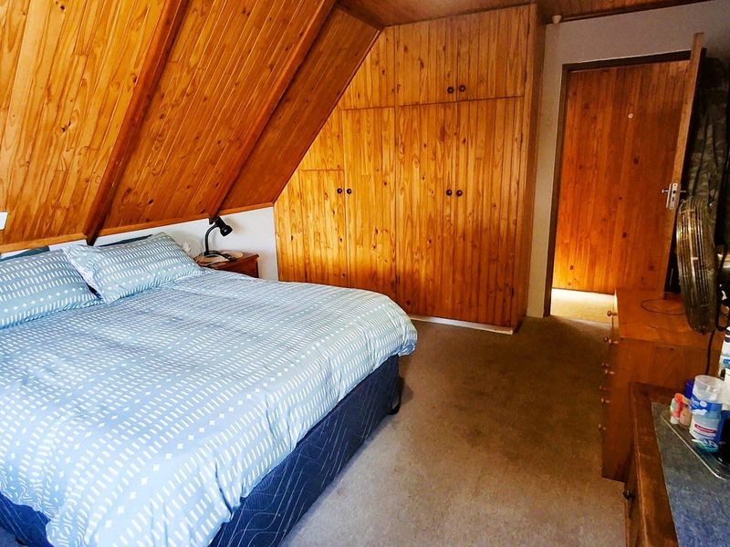 A bedroom featuring sloped timber ceilings, wood-paneled walls, and built-in wooden cabinetry, offering a rustic aesthetic.