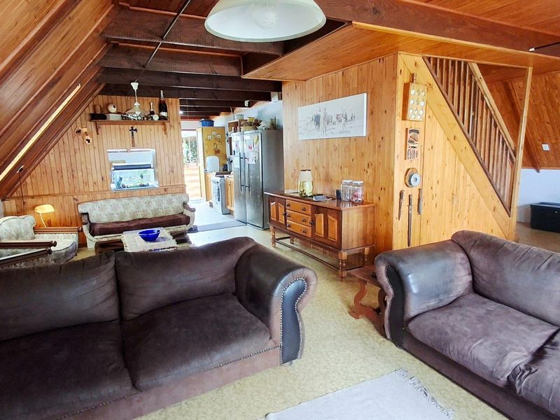 Open-plan living area featuring extensive timber wall paneling, exposed beams, and an integrated staircase, creating a rustic, cabin-style atmosphere.