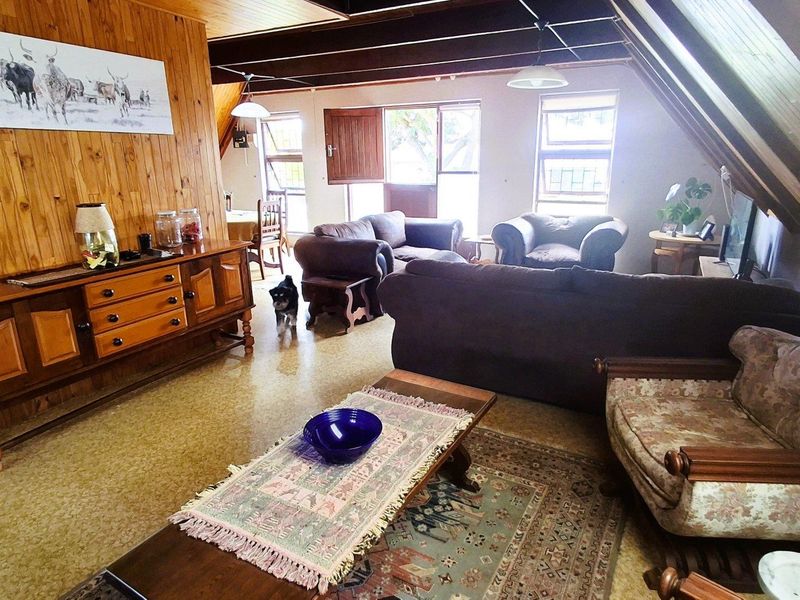 Spacious living area featuring exposed timber ceiling beams, warm wood wall paneling, and large windows providing natural light.