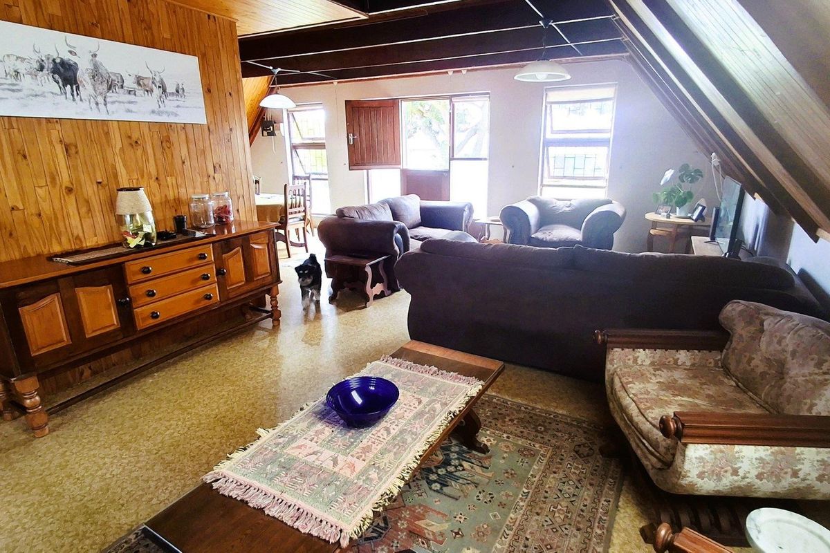 Spacious living area featuring exposed timber ceiling beams, warm wood wall paneling, and large windows providing natural light.