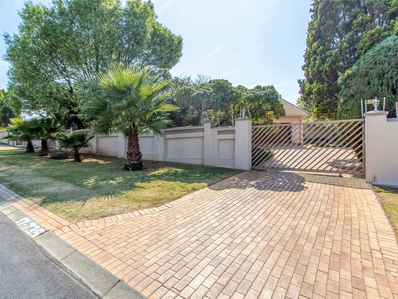 Front view of the property featuring a paved driveway, secure perimeter wall with electric fencing, and a well-maintained garden area.