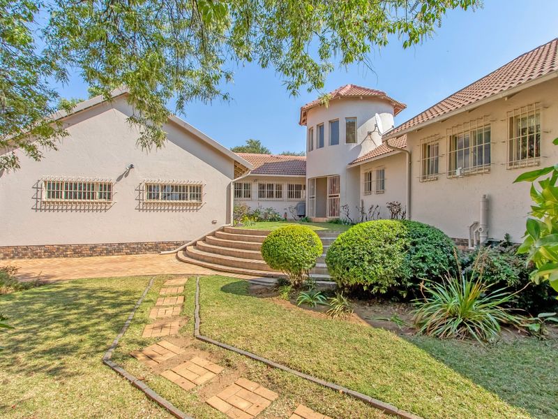 Rear view of the property featuring a unique turret design, curved concrete steps, paved pathways, and established garden landscaping.