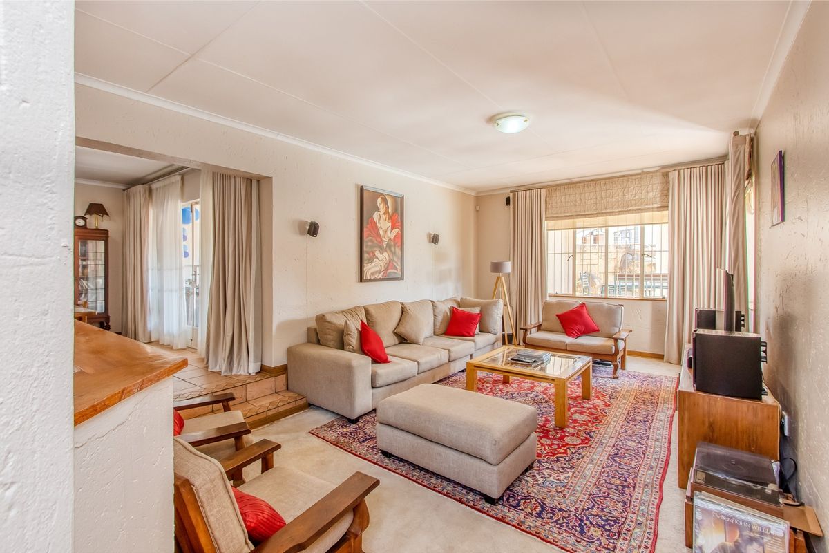 A spacious living room featuring a raised tiled step area, neutral wall finishes, and large windows with security bars.