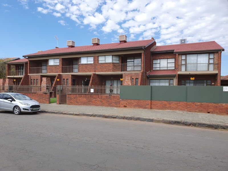 A street-level view of a multi-unit townhouse complex featuring red brick construction, tiled roofing, and private balconies for each unit.
