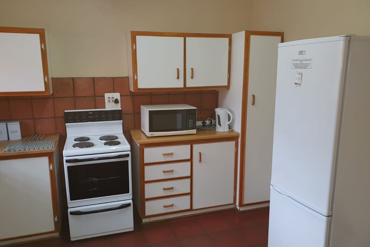 A functional kitchen featuring white cabinetry with wood trim, a freestanding electric stove, and terracotta-style floor tiles.