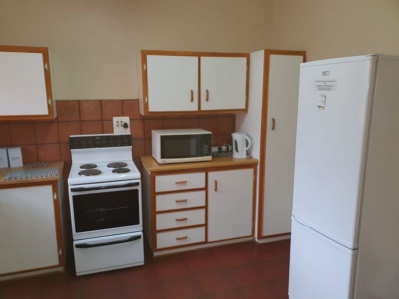 A functional kitchen featuring white cabinetry with wood trim, a freestanding electric stove, and terracotta-style floor tiles.