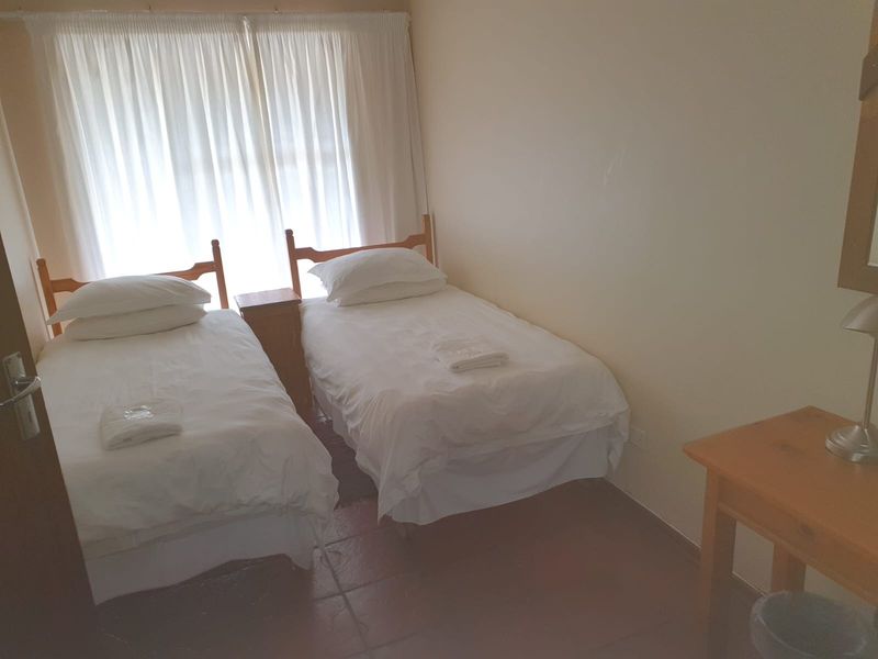 A functional bedroom featuring tiled flooring and large windows with curtain tracks, providing a simple and practical living space.