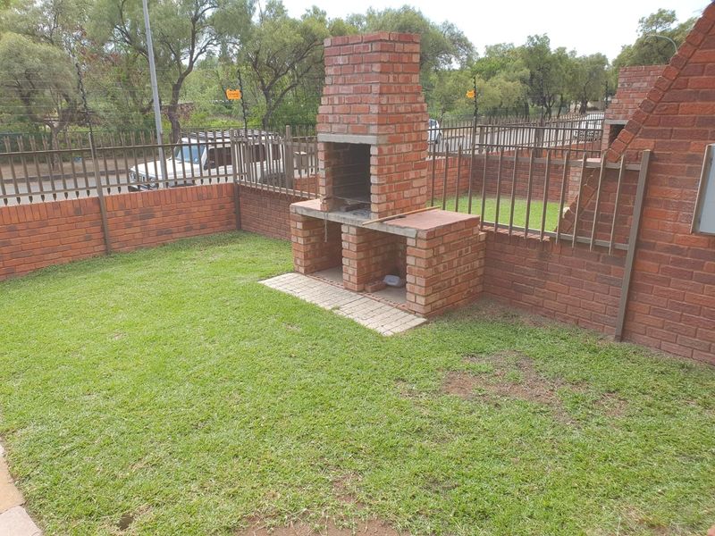 A private garden area featuring a built-in brick braai, enclosed by brick perimeter walls and metal security fencing with electric wiring.