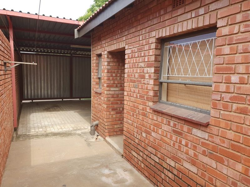 A view of the rear exterior featuring face brick walls, a covered carport area, and security bars on the windows.