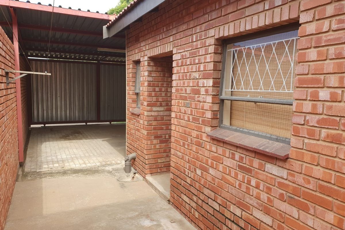 A view of the rear exterior featuring face brick walls, a covered carport area, and security bars on the windows.