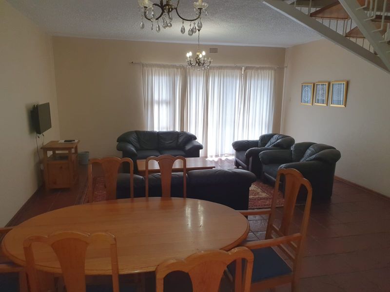 Spacious open-plan living and dining area featuring tiled flooring, a staircase, and large sliding doors providing natural light.