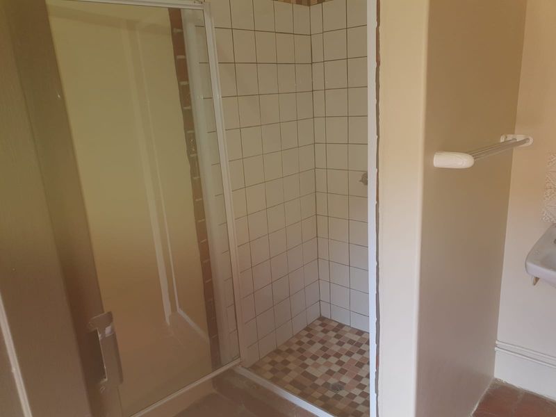 A functional bathroom featuring a shower enclosure with tiled walls and floor, a wall-mounted basin, and a towel rail, requiring some cosmetic updates.
