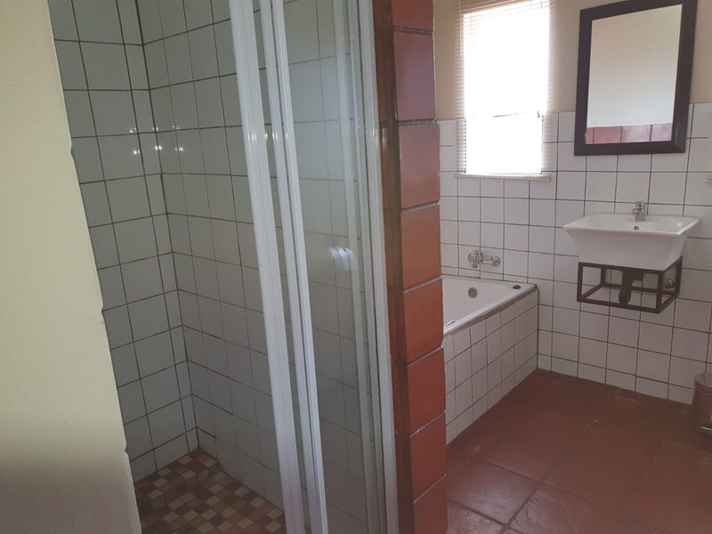 A functional bathroom featuring a separate shower enclosure, a bathtub, and a wall-mounted basin with tiled finishes throughout.