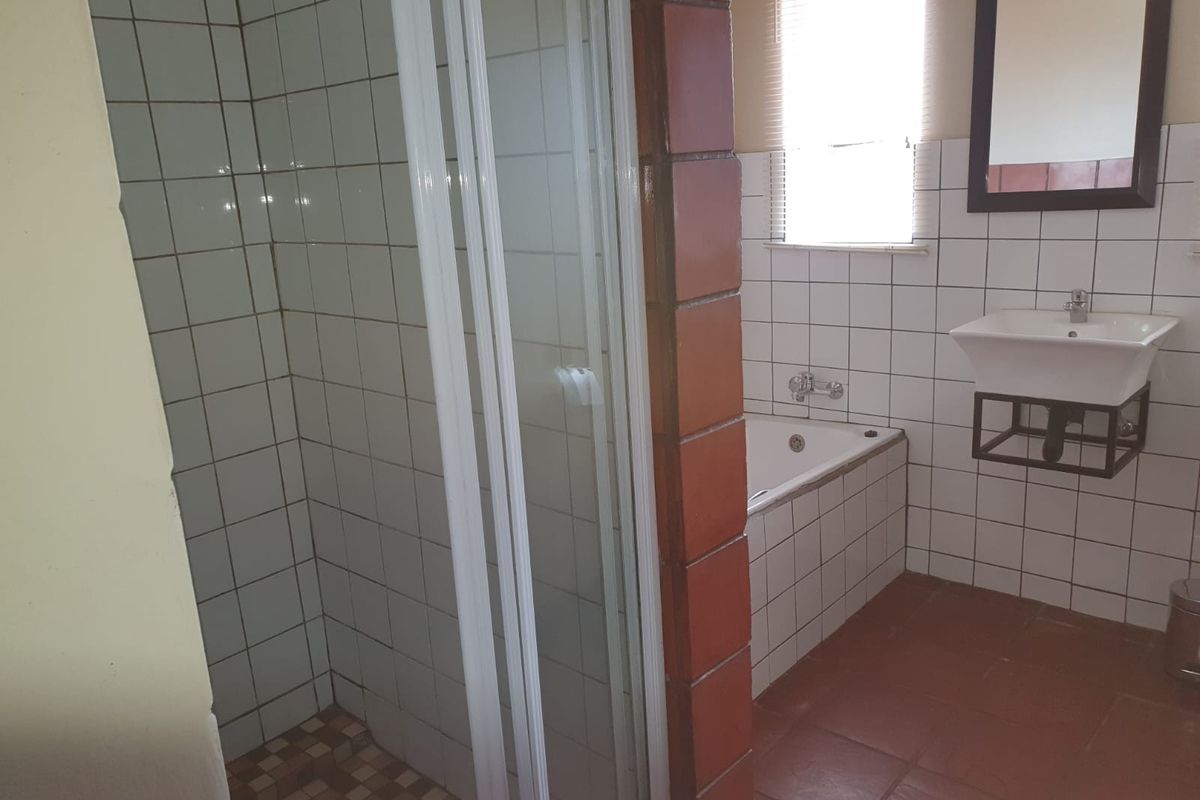 A functional bathroom featuring a separate shower enclosure, a bathtub, and a wall-mounted basin with tiled finishes throughout.