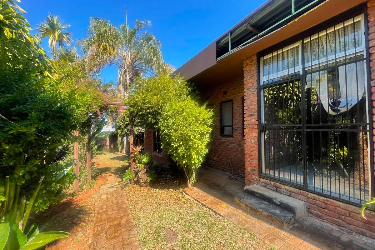 Rear exterior view of a brick house featuring a paved walkway, security-barred windows, and a timber pergola set within a landscaped garden.