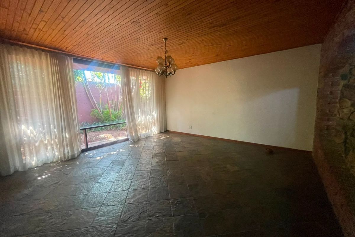 Spacious living area featuring a timber ceiling, slate tile flooring, and a stone feature wall with large windows overlooking the garden.