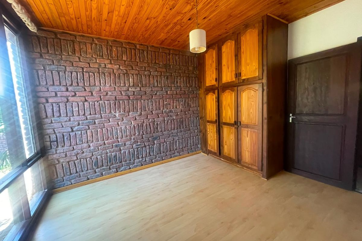 A bedroom featuring a rustic exposed brick wall, timber ceiling, laminate flooring, and built-in wooden cupboards.