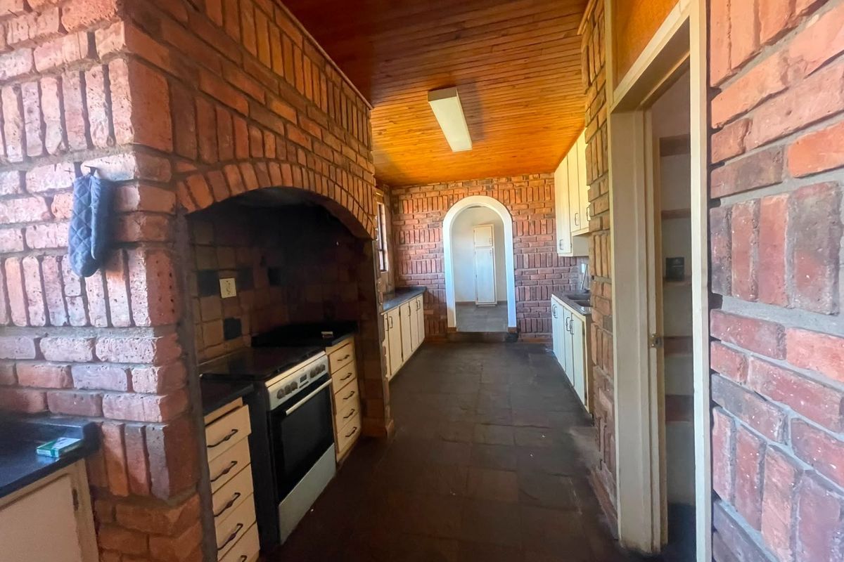 A dated kitchen featuring exposed brick walls, timber ceiling, and built-in cabinetry with a traditional brick-enclosed stove area.