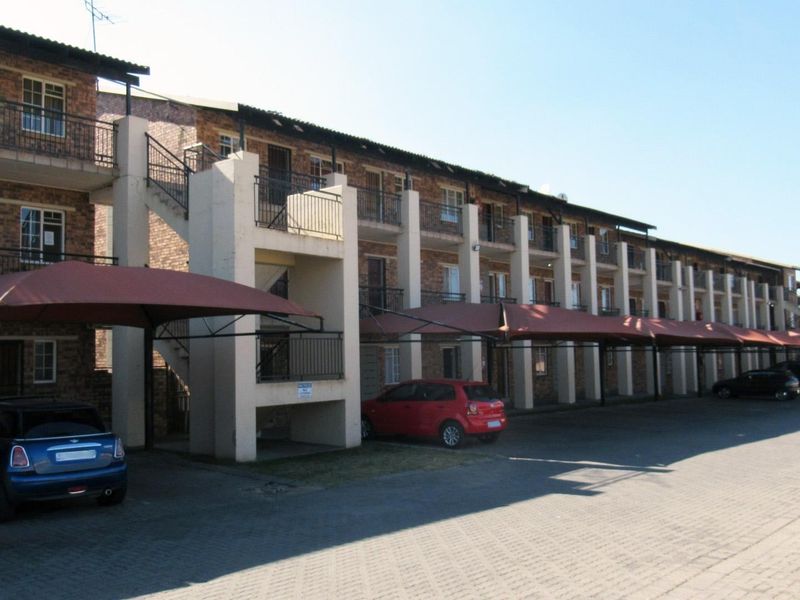 Exterior view of a multi-story apartment complex featuring brick facade, private balconies, external staircases, and covered parking bays.