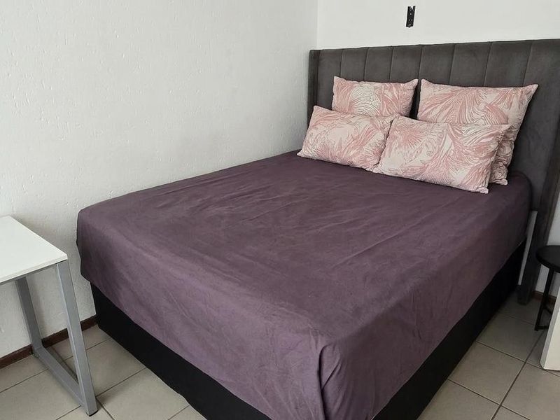 A compact bedroom featuring tiled flooring and a standard internal door, with visible wall damage above the bed area.