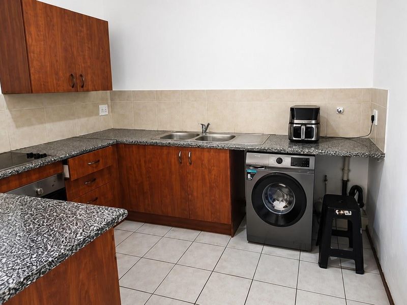 Functional kitchen featuring wood-finish cabinetry, granite countertops, a double basin sink, and integrated cooking appliances with tiled flooring and backsplash.