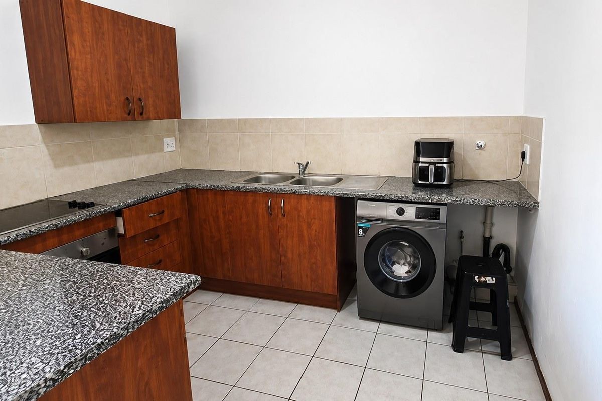 Functional kitchen featuring wood-finish cabinetry, granite countertops, a double basin sink, and integrated cooking appliances with tiled flooring and backsplash.