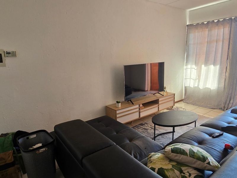 A living room featuring tiled flooring and a sliding glass door leading to an outdoor area, with an exposed electrical distribution board on the wall.