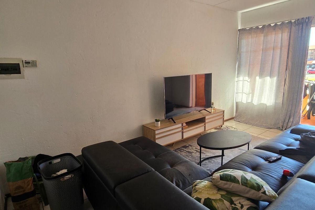 A living room featuring tiled flooring and a sliding glass door leading to an outdoor area, with an exposed electrical distribution board on the wall.