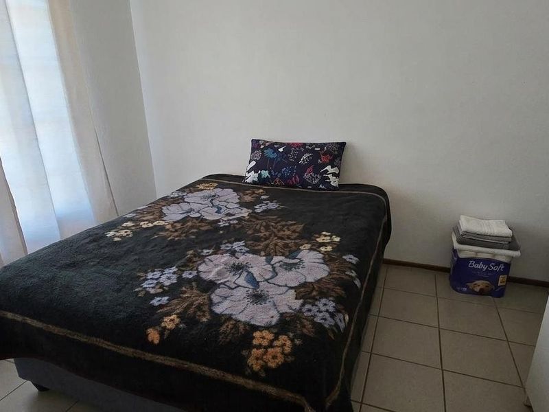 A simple bedroom featuring tiled flooring and a sliding door providing natural light.