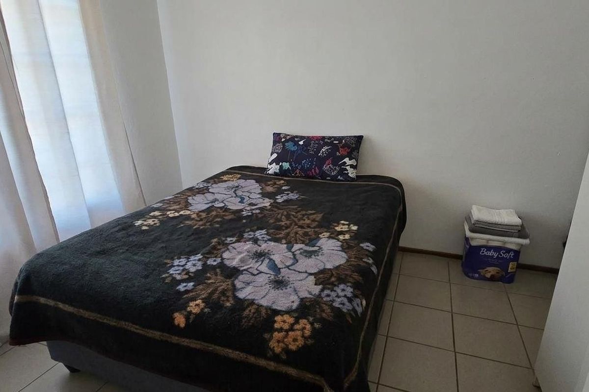 A simple bedroom featuring tiled flooring and a sliding door providing natural light.
