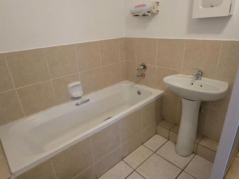 A functional bathroom featuring a pedestal basin, built-in bathtub, and separate shower enclosure with neutral ceramic tiling throughout.