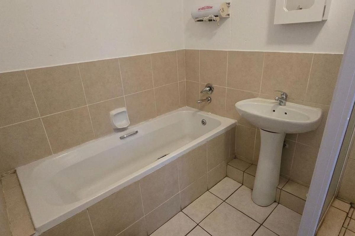 A functional bathroom featuring a pedestal basin, built-in bathtub, and separate shower enclosure with neutral ceramic tiling throughout.