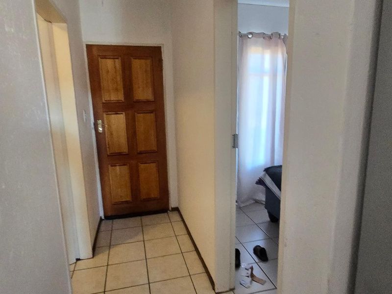 A functional hallway featuring tiled flooring and a wooden door, providing access to adjacent rooms within the apartment.