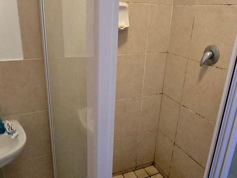 A compact bathroom shower enclosure featuring tiled walls and flooring, currently showing signs of wear and grout discoloration.