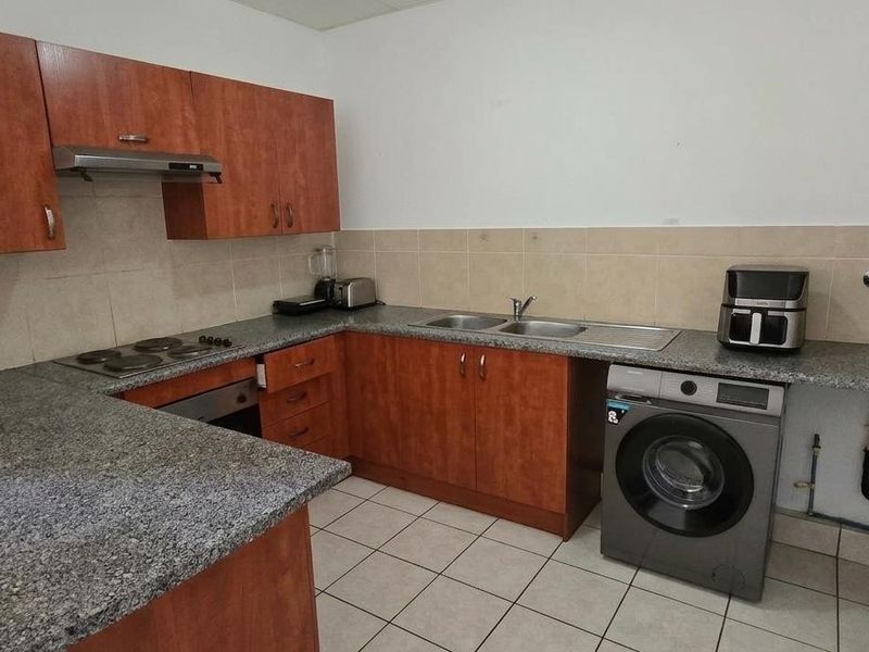 Functional kitchen featuring granite countertops, built-in oven, electric hob, extractor fan, and dedicated plumbing for a washing machine.