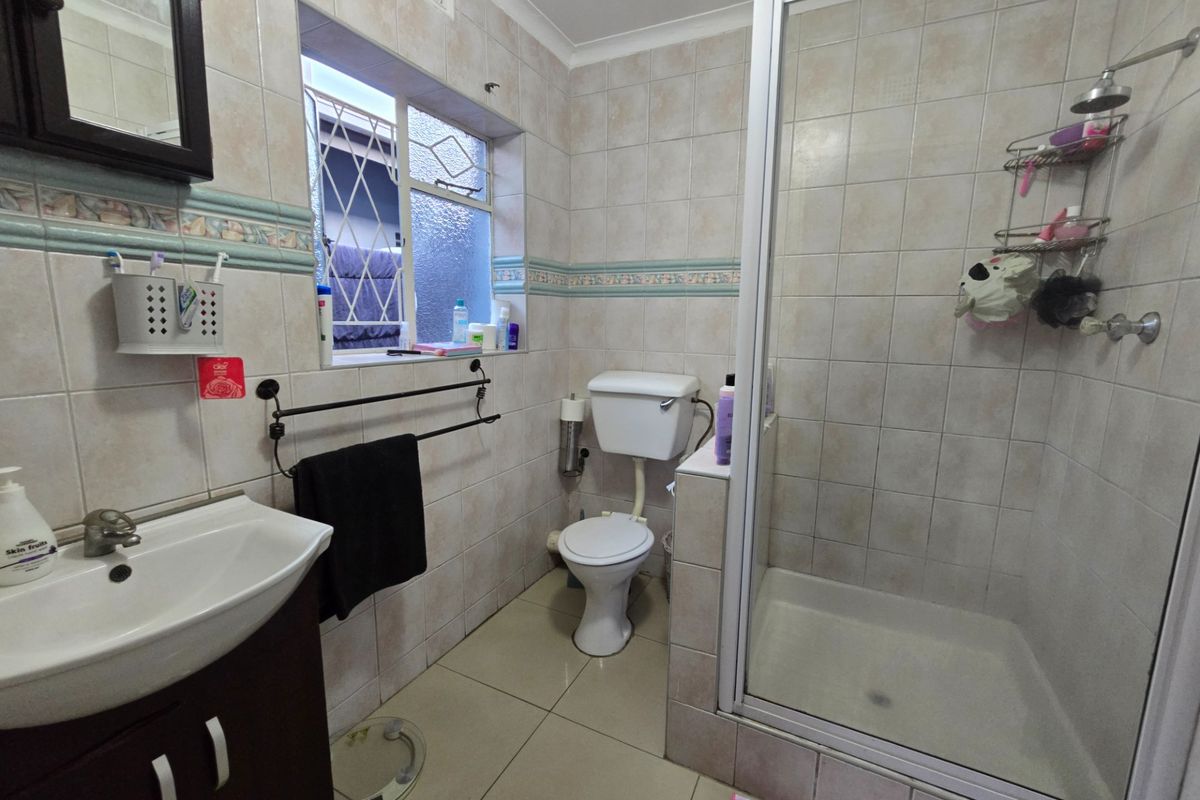 A functional bathroom featuring a shower enclosure, vanity basin, and toilet with neutral wall and floor tiling.