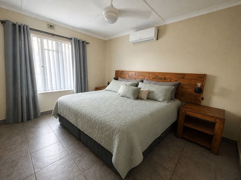 A well-maintained bedroom featuring tiled flooring, a ceiling fan, and a wall-mounted split-system air conditioner.