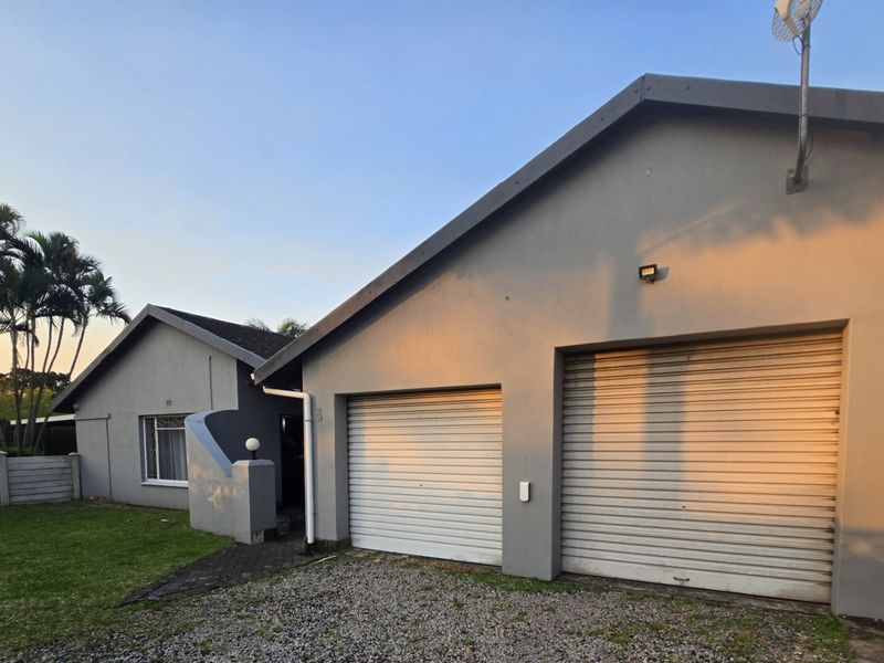 Front view of the property featuring a double garage with roller shutter doors, a paved driveway, and a precast boundary wall.