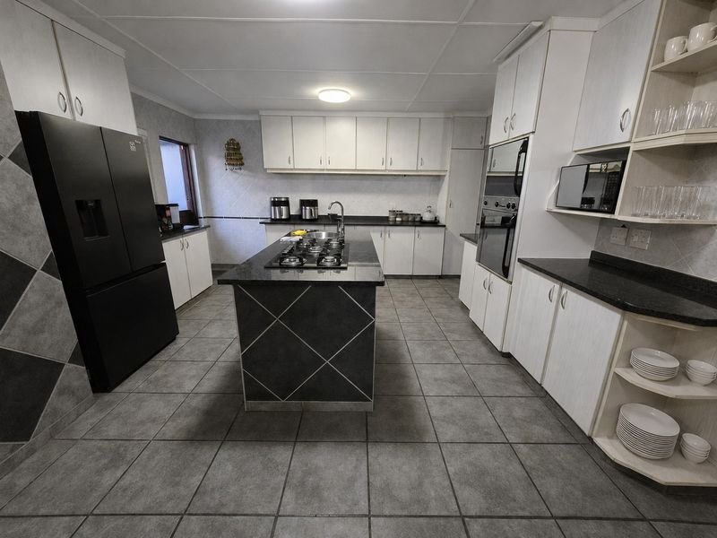 Spacious kitchen featuring a central island with a gas hob, granite countertops, built-in oven, microwave, and ample cabinetry for storage.