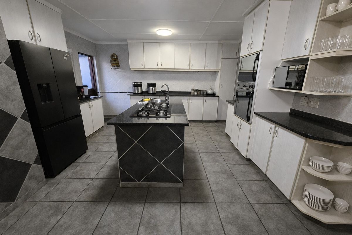 Spacious kitchen featuring a central island with a gas hob, granite countertops, built-in oven, microwave, and ample cabinetry for storage.