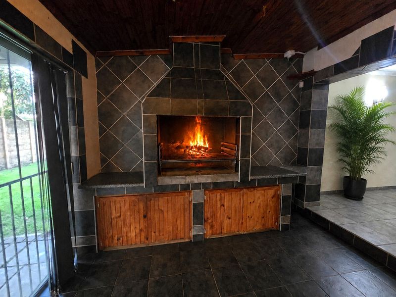 Covered patio area featuring a large built-in braai with tiled surround, wooden ceiling, and direct access to the garden through sliding glass doors.