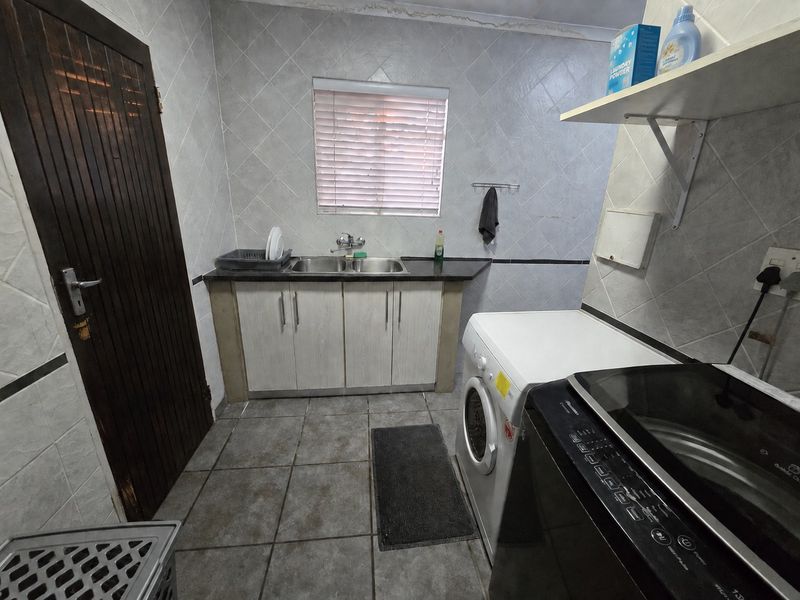 Functional laundry room featuring tiled walls and flooring, built-in cabinetry with a double basin sink, and dedicated space for laundry appliances.