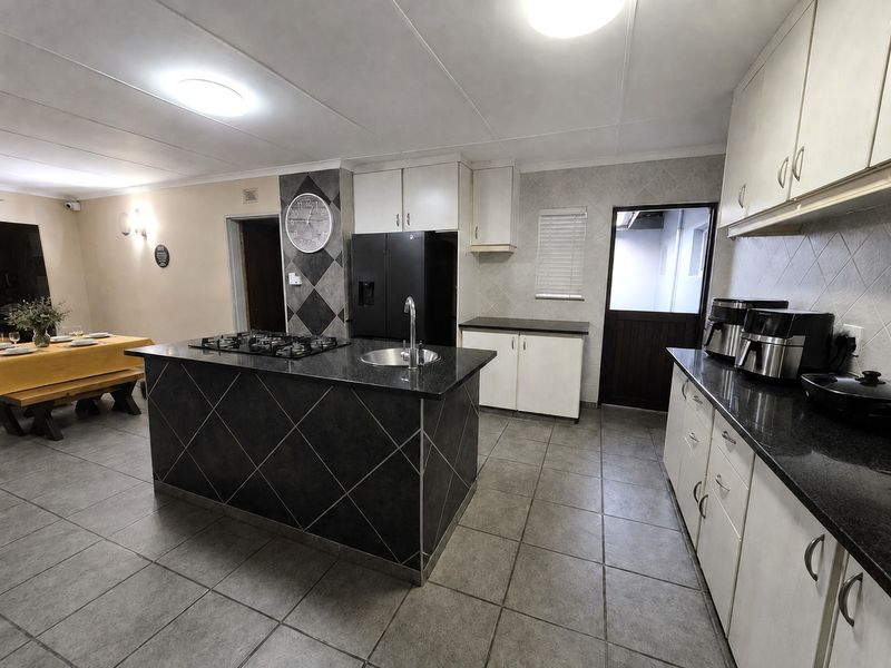 Open-plan kitchen featuring a central island with a gas hob and sink, granite countertops, and tiled flooring, seamlessly connecting to the dining area.