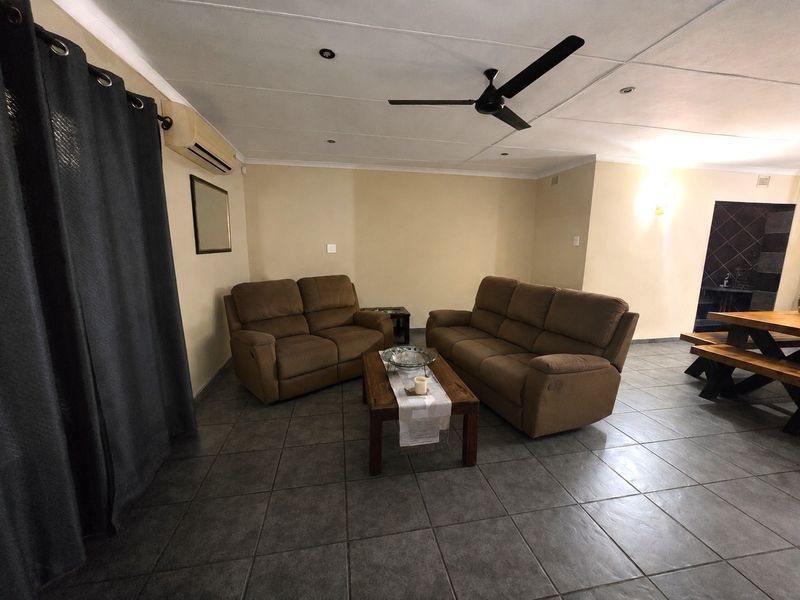 A spacious living area featuring tiled flooring, a ceiling fan, and a wall-mounted air conditioning unit.