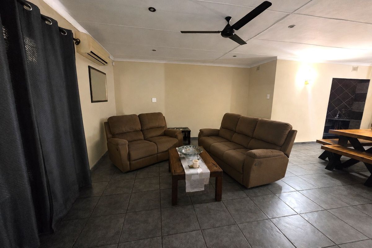 A spacious living area featuring tiled flooring, a ceiling fan, and a wall-mounted air conditioning unit.