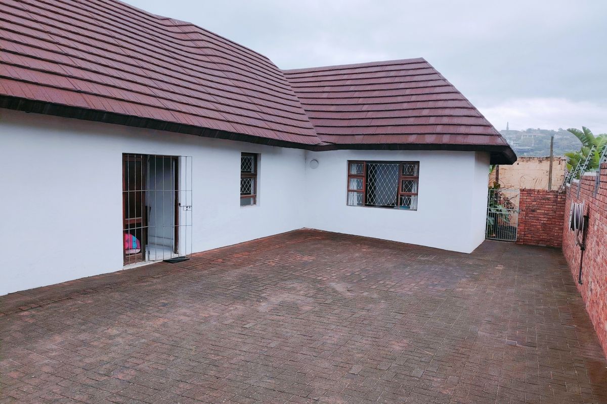 A rear exterior view of the house featuring a tiled roof, paved courtyard area, and secure window and door fittings.