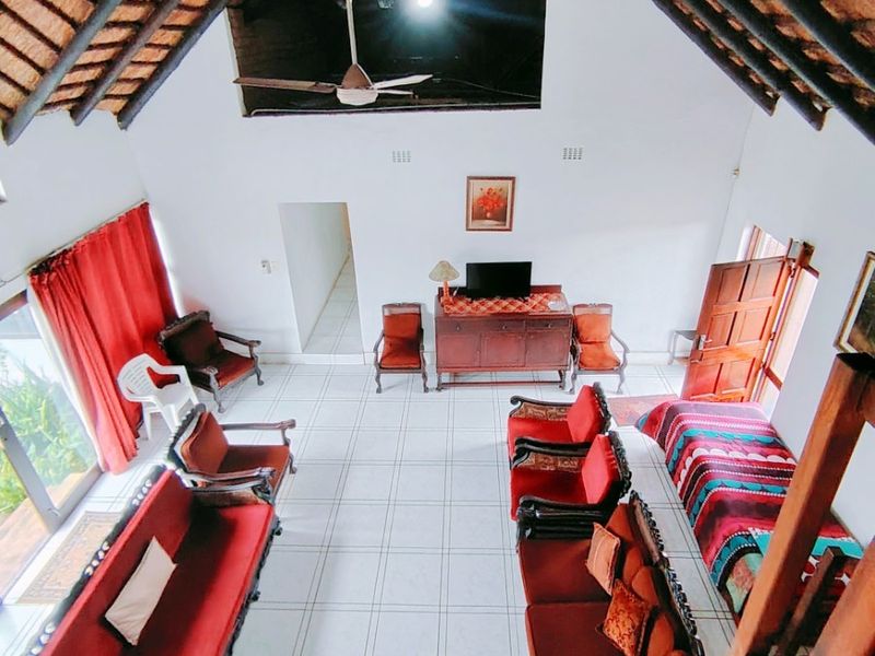 Spacious living area featuring a high vaulted thatch ceiling with exposed timber rafters, tiled flooring, and large sliding doors providing natural light.