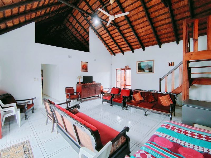 Spacious living room featuring a high vaulted thatched ceiling with exposed timber rafters, ceramic tiled flooring, and a wooden staircase leading to an upper level.