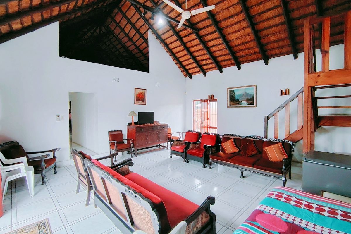 Spacious living room featuring a high vaulted thatched ceiling with exposed timber rafters, ceramic tiled flooring, and a wooden staircase leading to an upper level.